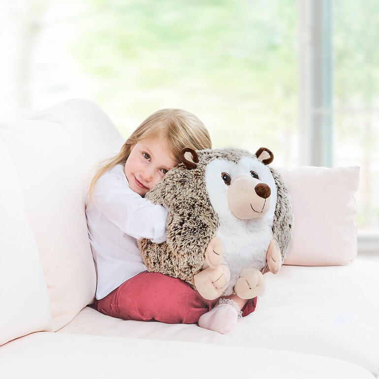 Enfant embrassant un coussin chauffant en forme de hérisson dans un cadre confortable