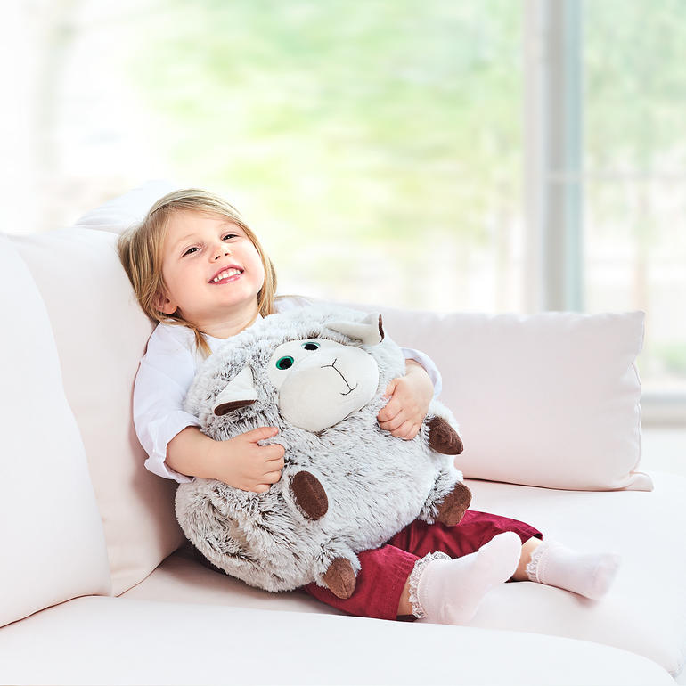 Enfant qui étreint un coussin chauffant en forme de mouton sur un canapé