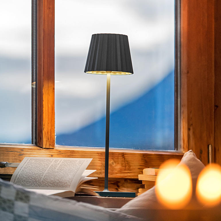 Lampe de table rechargeable noire, sur une table près d'un rebord de fenêtre.