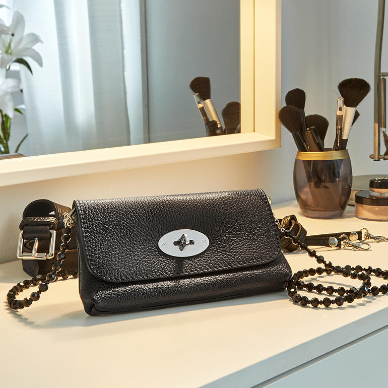 Sac ceinture noir en cuir sur une table de maquillage, avec des cosmétiques.