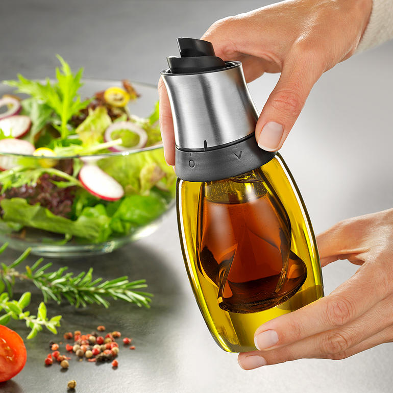 Il suffit de faire pivoter le couvercle pour choisir entre huile et vinaigre. Personne tenant une bouteille d'huile et de vinaigre au-dessus d'une salade dans un bol.