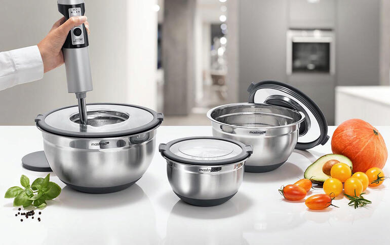 Trois bols en acier inoxydable de différentes tailles avec des ustensiles de cuisine sur un plan de travail.