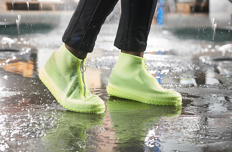 Personne avec des surchaussures de pluie vertes claires se tient dans une flaque.