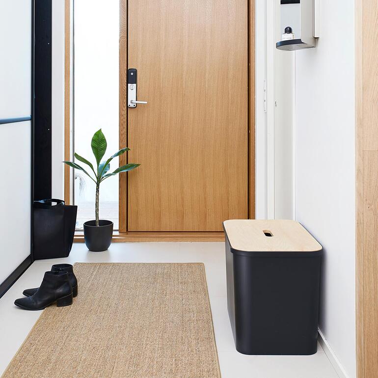 Conteneur à déchets noir dans l'entrée à côté d'une plante