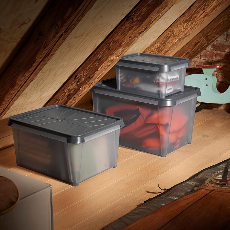 Trois boîtes de rangement transparentes dans un grenier, remplies de divers objets.