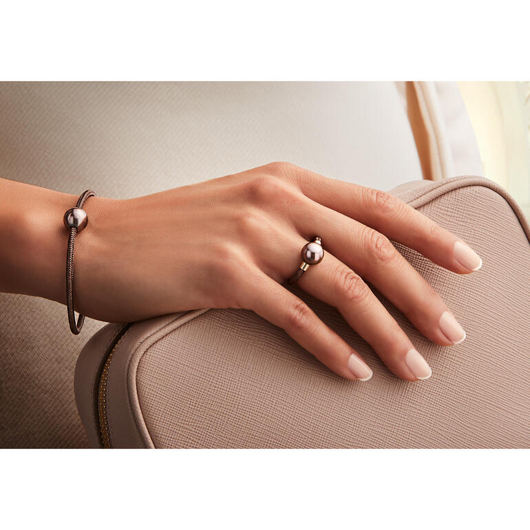 Main tenant un bracelet et une bague en or rose avec perle noire sur un sac.