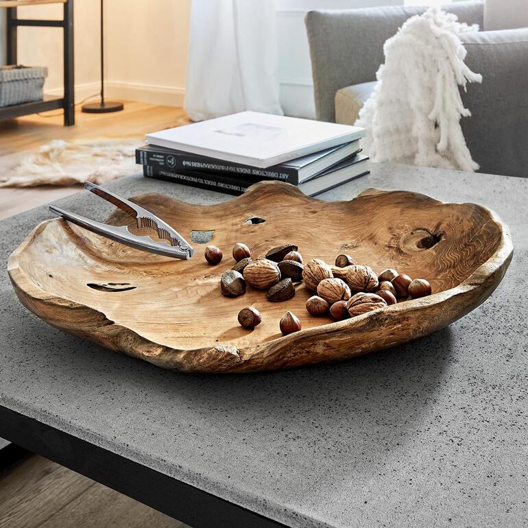 Bol en teck à côté de noix et d'une pince sur une table.