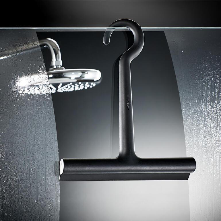 Raclette de douche en silicone design accrochée à une porte en verre dans la salle de bain.
