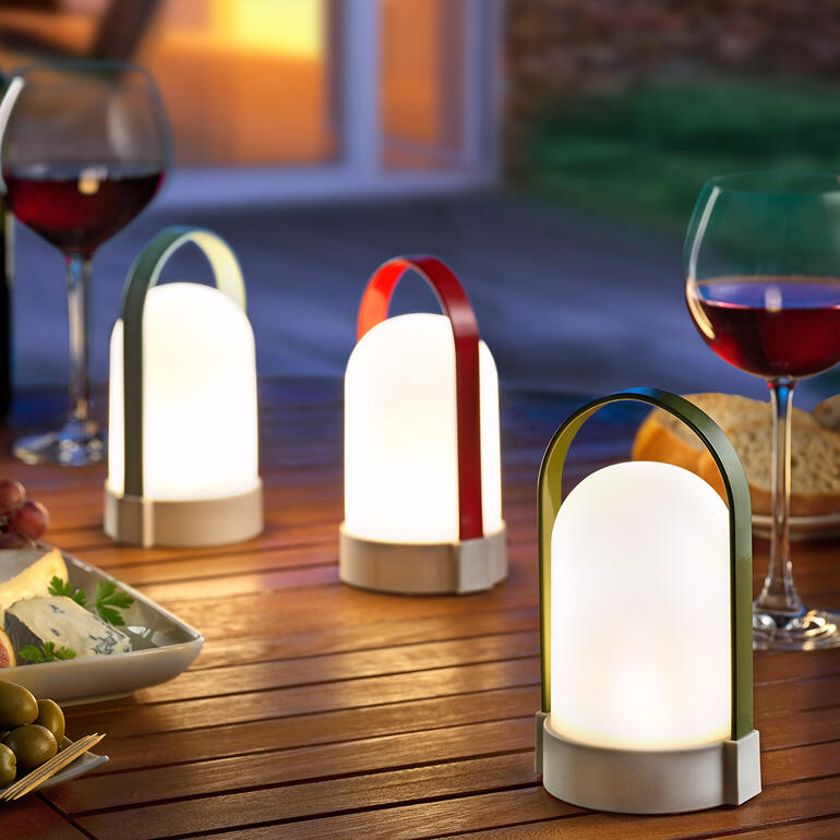 Trois lampes à piles Piccolos sur une table à l'extérieur, entourées de nourriture.