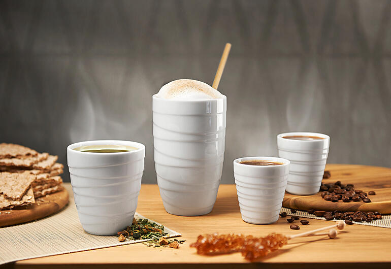 Quatre tasses thermiques en porcelaine sur une table, entourées de collations.