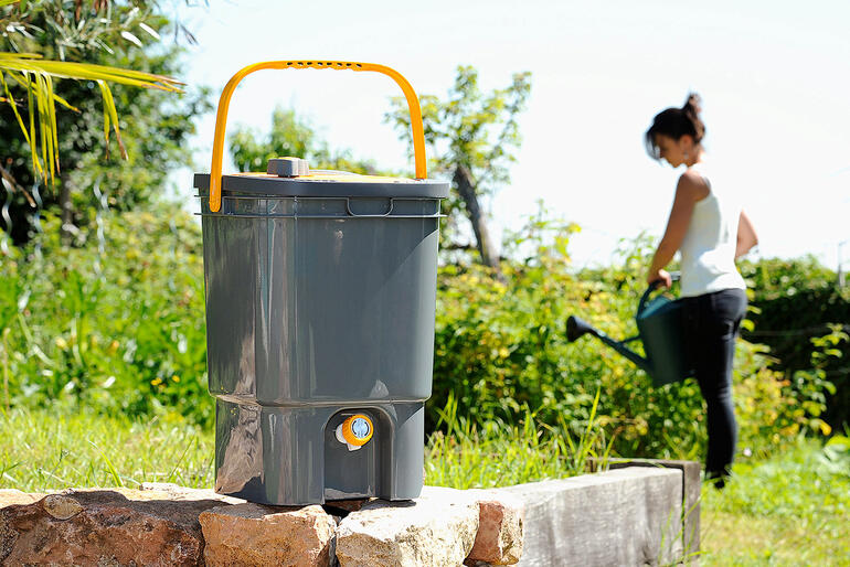 Préparateur de fertilisant liquide BioMix dans un jardin, femme travaillant en arrière-plan.