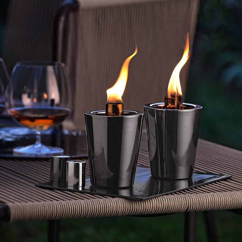 Torches de table sur une table dans un espace extérieur avec un verre à cocktail en arrière-plan.