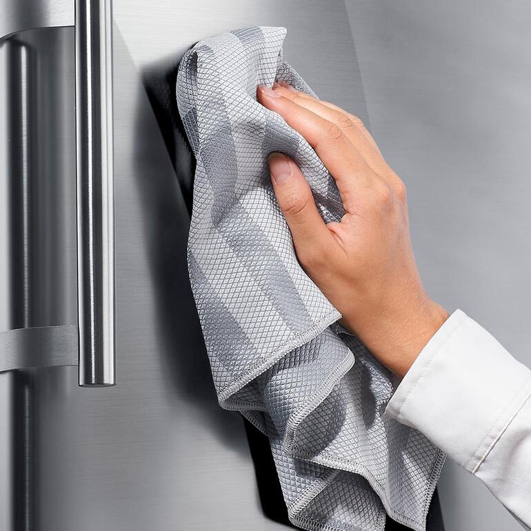 Chiffons universels, lot de 10 pièces Une main nettoie un réfrigérateur en acier inoxydable avec un chiffon universel gris.