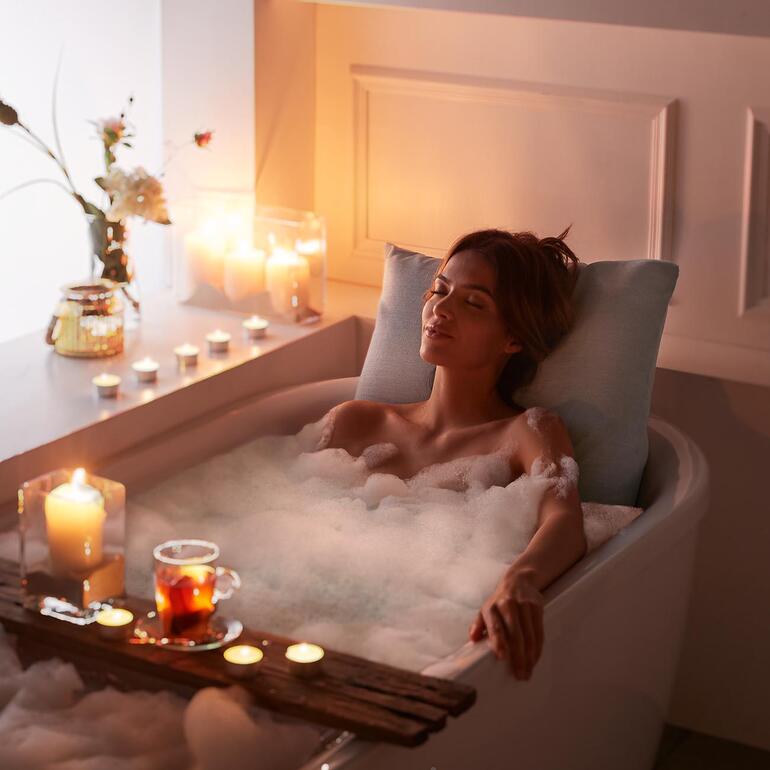 Femme se détend dans le bain avec un coussin de bain et des bougies autour.