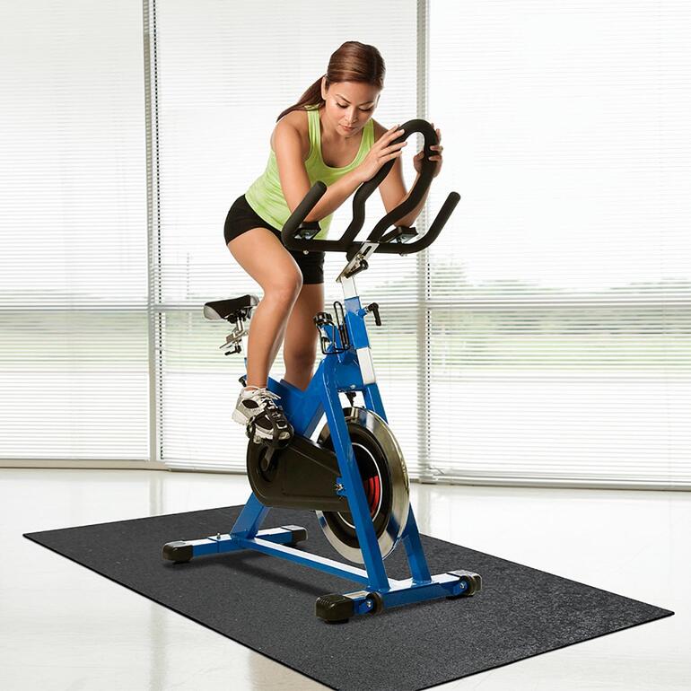 Femme sur un vélo stationnaire sur un tapis de protection en recyclage.