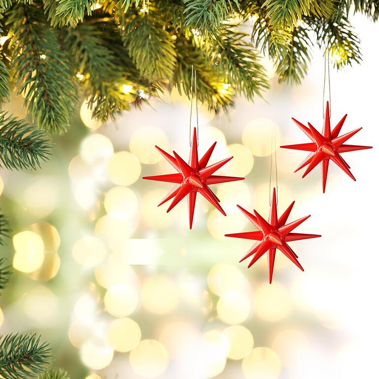Trois étoiles de Noël Seiffen rouges suspendues à un sapin décoré.