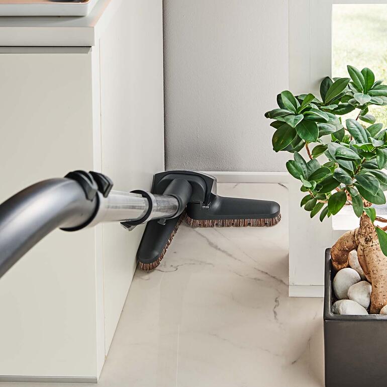 Dans les coins et les niches, le suceur Flex se plie et se déplie en douceur – plus besoin de vous baisser ni de déplacer les meubles. Buse d’aspirateur flexible utilisée dans un coin d'une pièce.