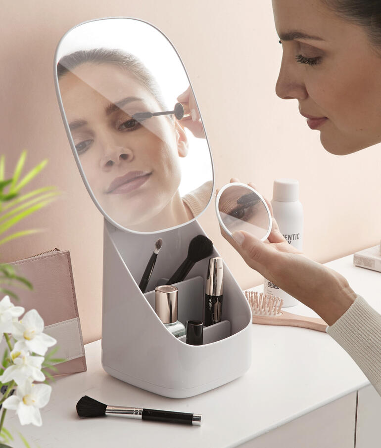 Femme se maquillant devant un miroir de maquillage avec organisateur intégré sur une table.