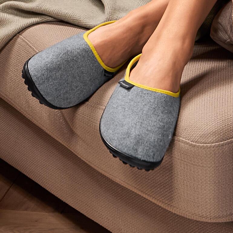 Deux pantoufles en feutre de laine grises leguano® sur un canapé.