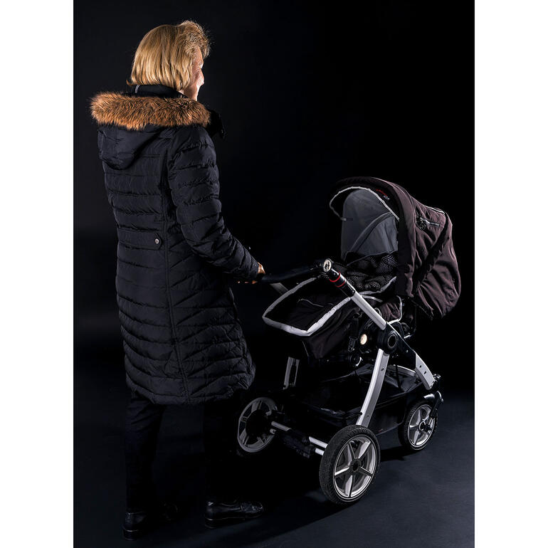 Sans housse de sécurité pour landau. Femme avec une poussette sans gilet avertisseur, sur un fond sombre.