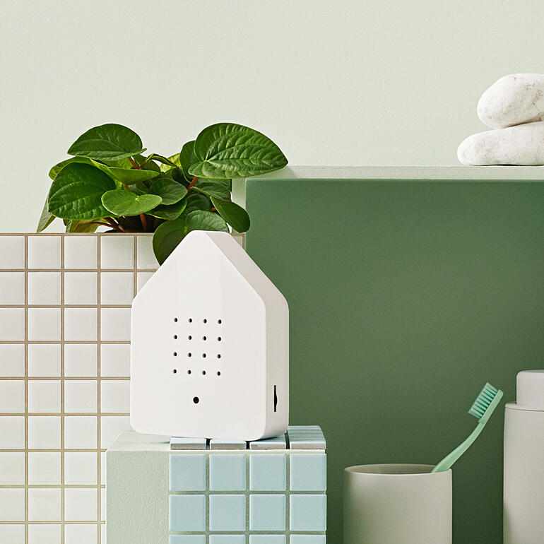 Dispositif Zwitscherbox blanc à côté de plantes et d'accessoires de salle de bain sur une étagère.