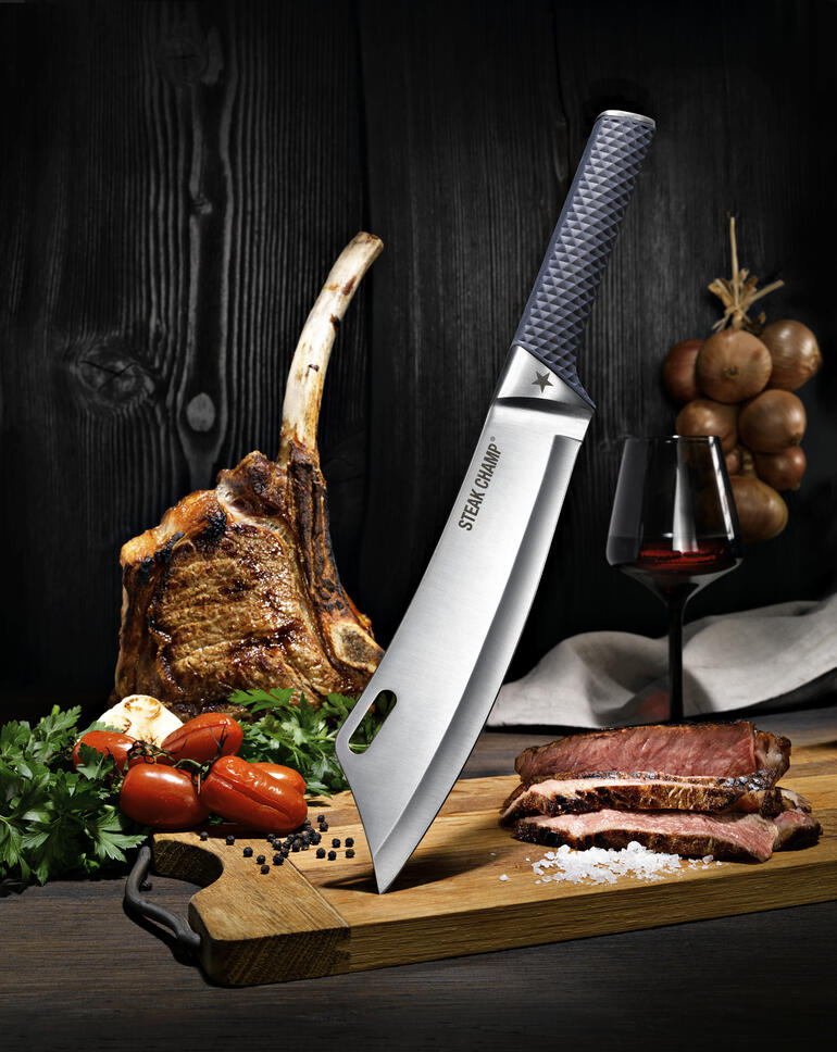 Couteau de cuisine BBQ pro SteakChamp Couteau de cuisine SteakChamp sur une planche à découper, à côté d'un morceau de viande et d'une bouteille de vin.