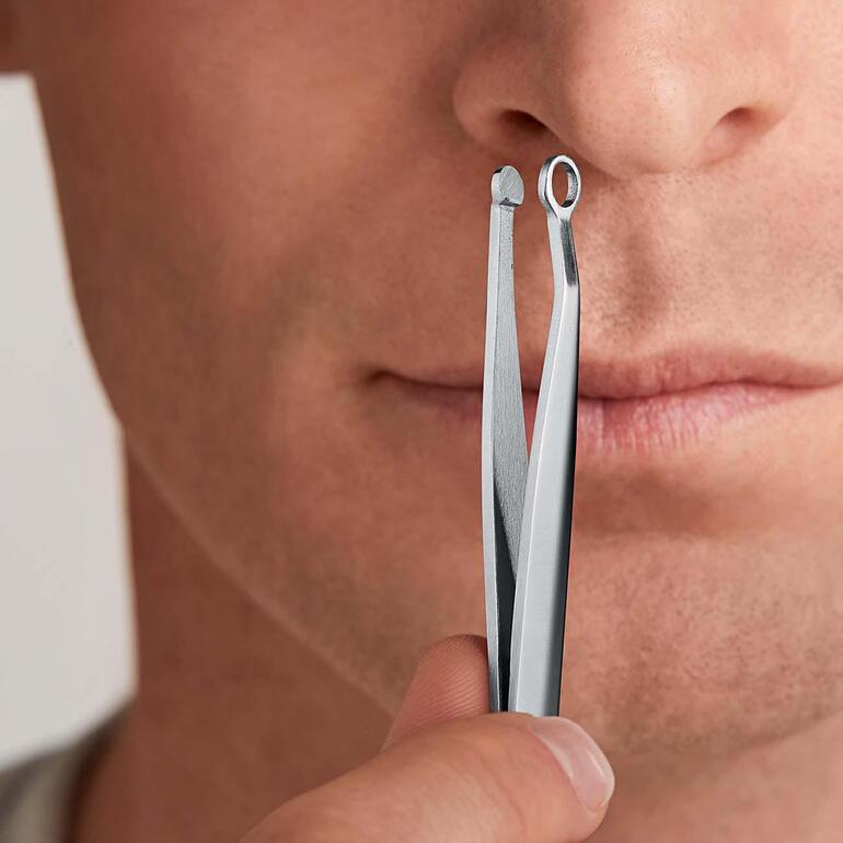 Homme tenant une pince à épiler pour le nez devant son visage.