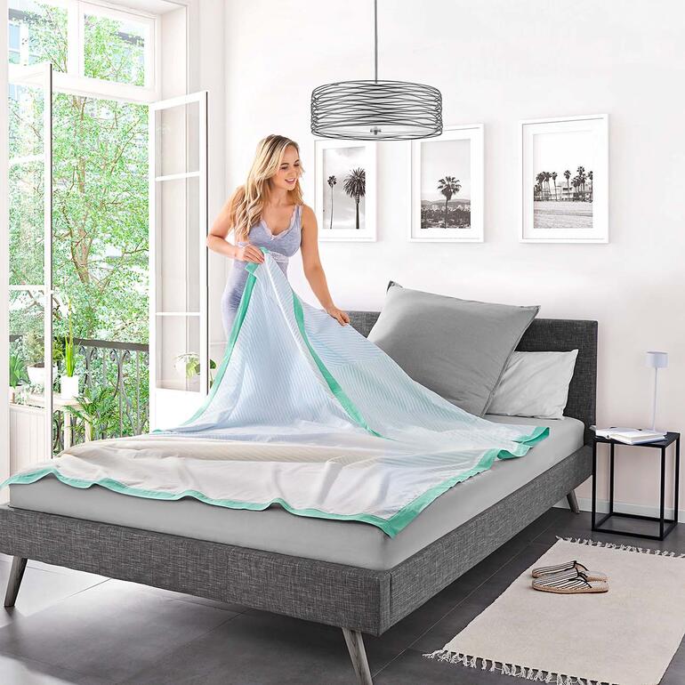 Femme pliant la Breezyblanket sur un lit.