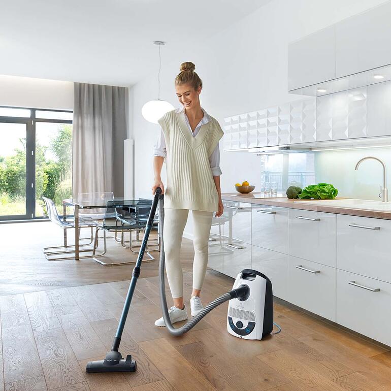 Femme utilise un aspirateur à sol dans un coin cuisine moderne.