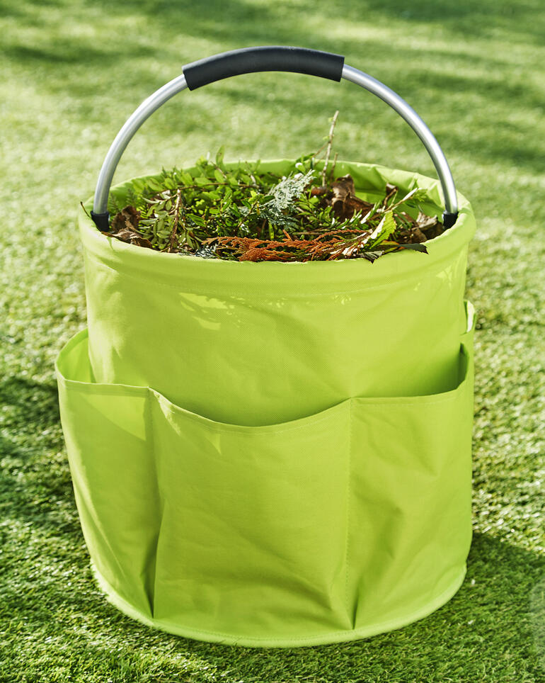 Un équipement parfait avec un compartiment central extra large de 28 l, 6 compartiments extérieurs spacieux et une poignée en alu rembourrée et puissante. Caddy de jardin rempli de déchets végétaux sur de l'herbe verte.