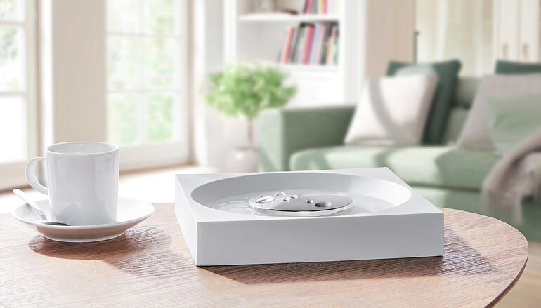 Neutraliseur de odeurs XL sur une table avec du café et un canapé en arrière-plan.