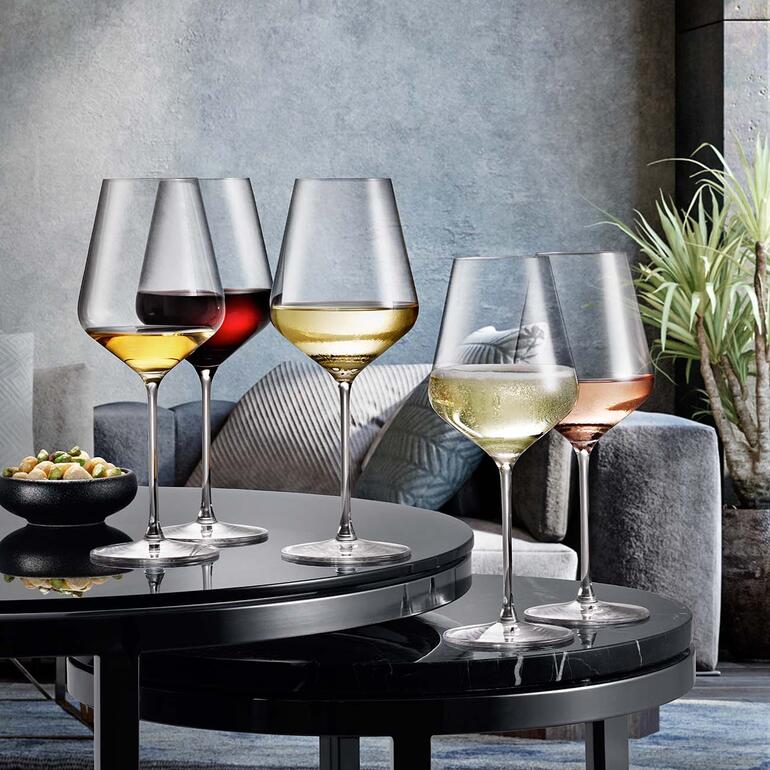 Quatre verres de vin de tailles différentes sur une table avec des collations en arrière-plan.