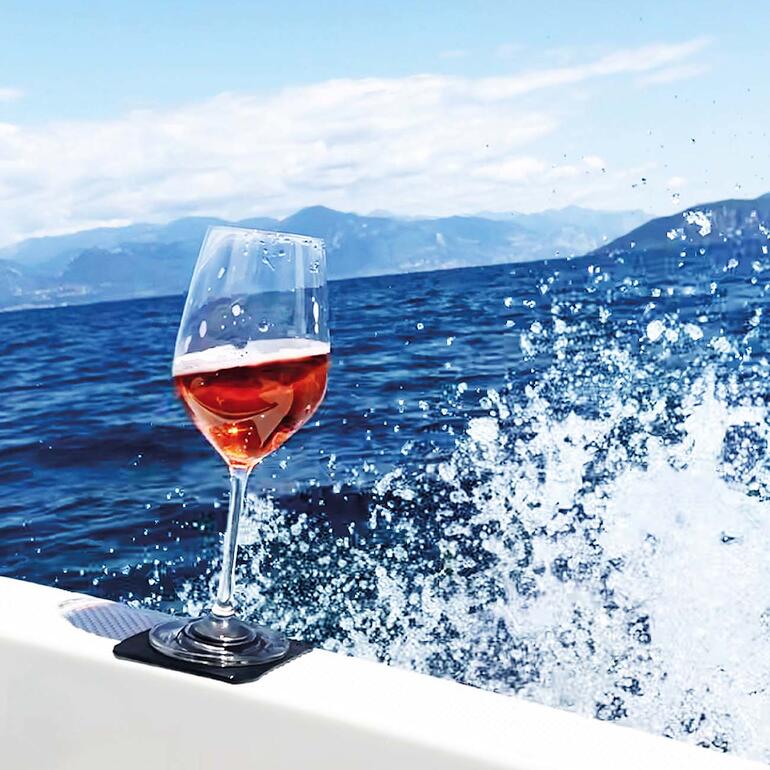 Verre de vin rosé sur un bateau devant un paysage côtier pittoresque