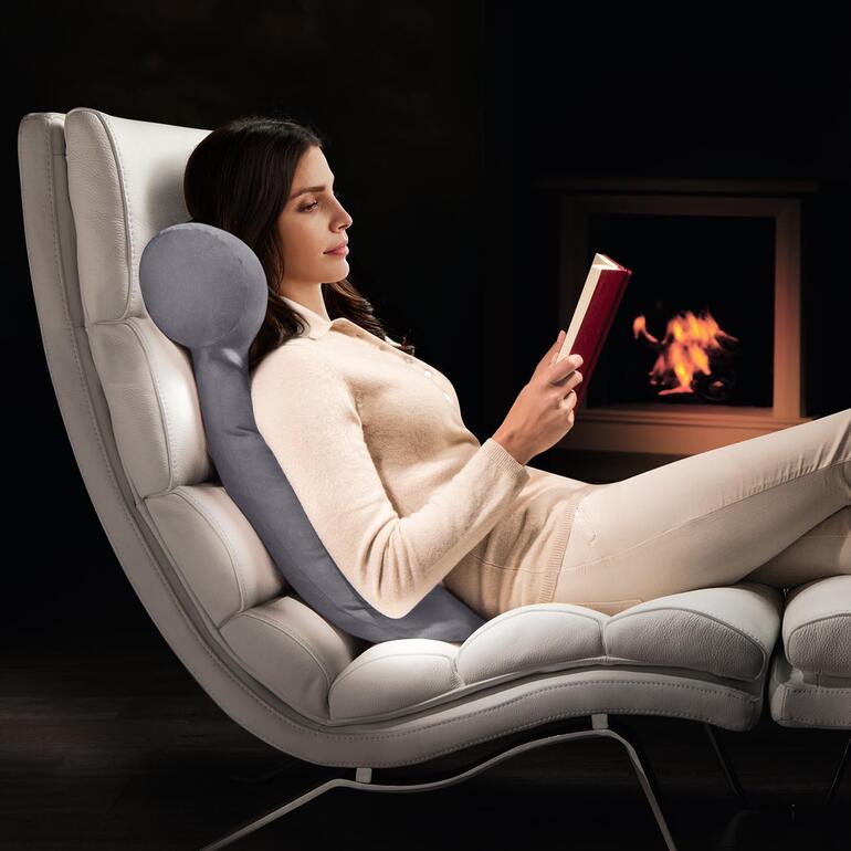 Femme se détendant dans un fauteuil et lisant avec un coussin de lecture HEFEL.
