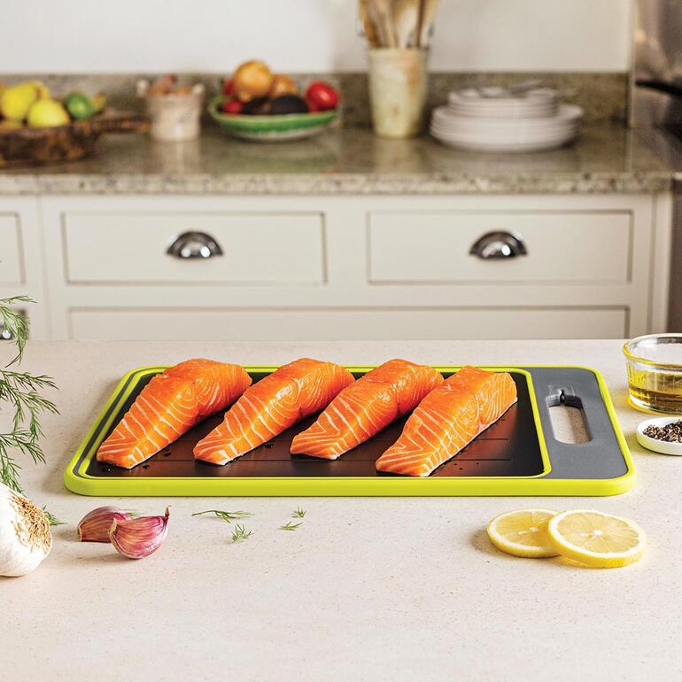 Lʼeau de décongélation sʼécoule rapidement et proprement dans la rigole collectrice. Filets de saumon sur une table de cuisine et une planche à découper.