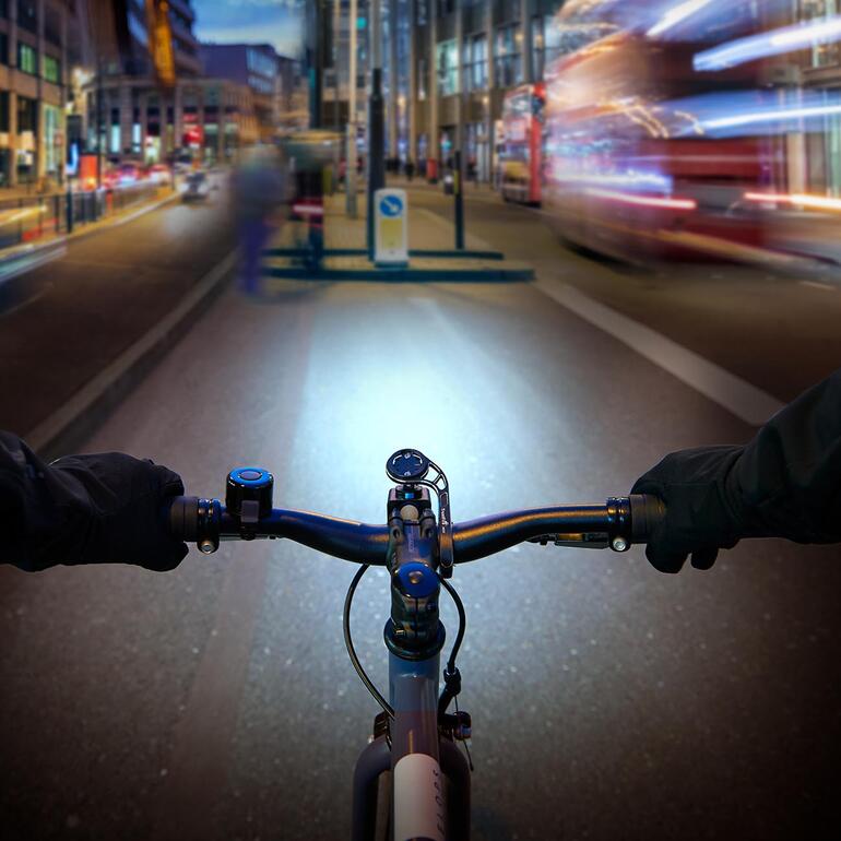 À positionner au milieu du guidon pour une optimisation supplémentaire de l’éclairage. Vue depuis le guidon d'un vélo sur une rue de la ville éclairée au crépuscule.