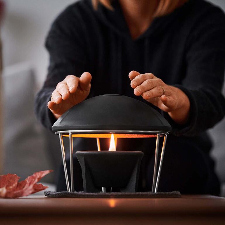 Cheminée de table et Cloche de chaleur Femme réchauffant ses mains sous le couvercle chauffant du schmelzfeuer.