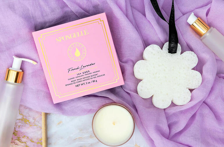 Éponge de beauté Spongellé dans un emballage rose, entourée de produits cosmétiques.