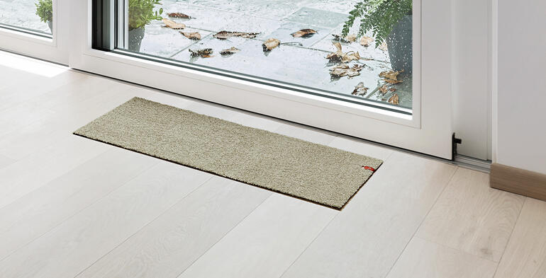 Tapis de porte de terrasse beige devant une porte vitrée.