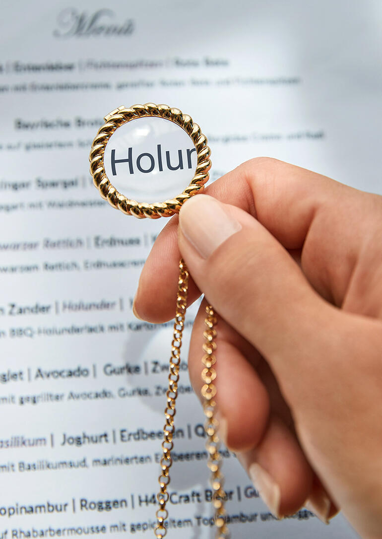 Main tenant une loupe à une chaîne dorée au-dessus d'un menu.