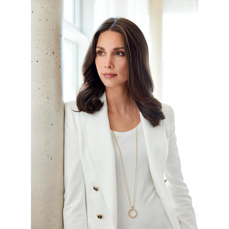 Lʼélégante chaîne avec pierre précieuse cristalline est également une loupe grossissante 6x. Femme en blazer blanc porte une chaîne avec une loupe autour du cou.