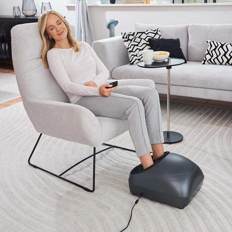 Femme se relaxant avec un appareil de massage des zones réflexes des pieds dans le salon.