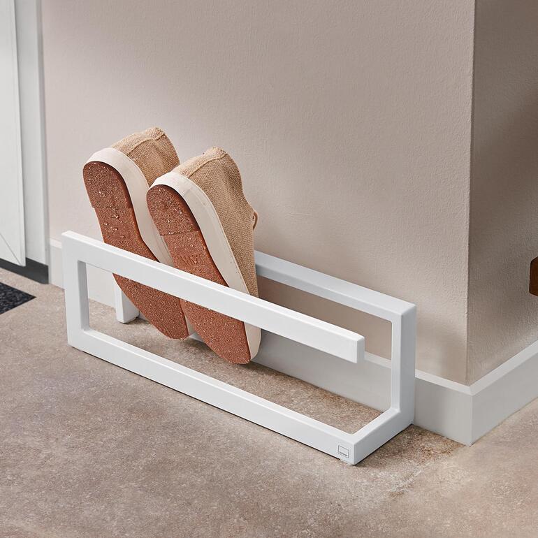 Étagère à chaussures avec une paire de baskets beiges sur une étagère blanche.
