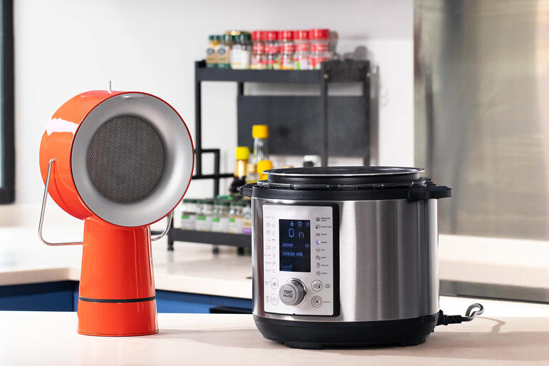 Hotte AirHood™ Appareil AirHood™ rouge à côté d'un autocuiseur sur un plan de travail.