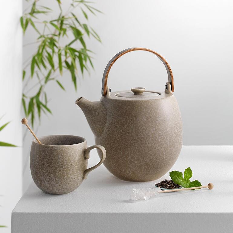 Théière et tasse en céramique grise sur une table avec une plante en arrière-plan