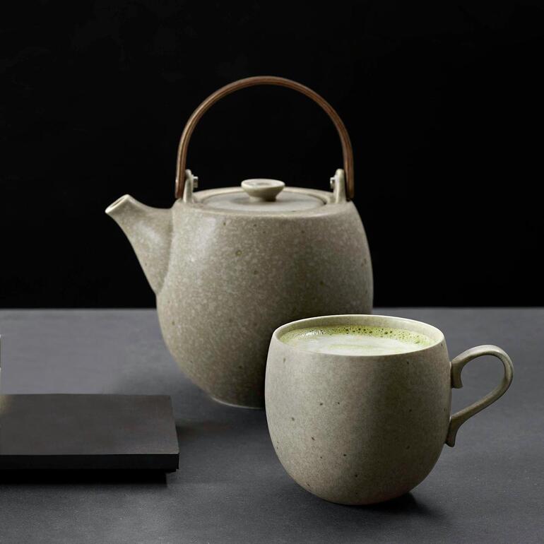 Théière et tasse en céramique grise sur une table sombre avec du thé vert dans la tasse