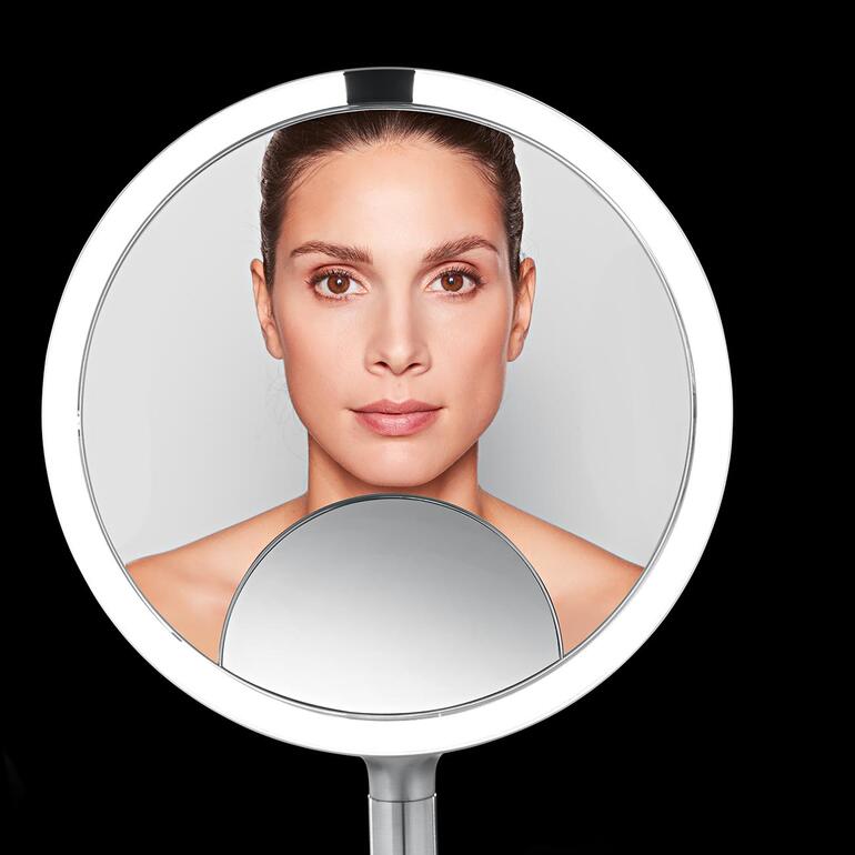 Vérifiez l’effet global de votre maquillage dans le miroir à vue générale, utilisez le côté du miroir avec un grossissement x5 pour corriger un trait d’eye-liner ou de crayon à lèvres et servez-vous de la fenêtre avec un grossissement x10 pour vérifier les plus petits détails. Gros plan d'un miroir cosmétique avec le visage d'une femme