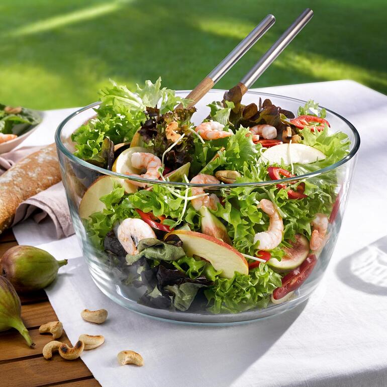 Grâce à la corbeille d’essorage amovible, vous pouvez servir la salade rincée directement dans l’élégant saladier en verre de borosilicate, clair comme du cristal. Bol avec de la salade fraîche sur une table en extérieur.