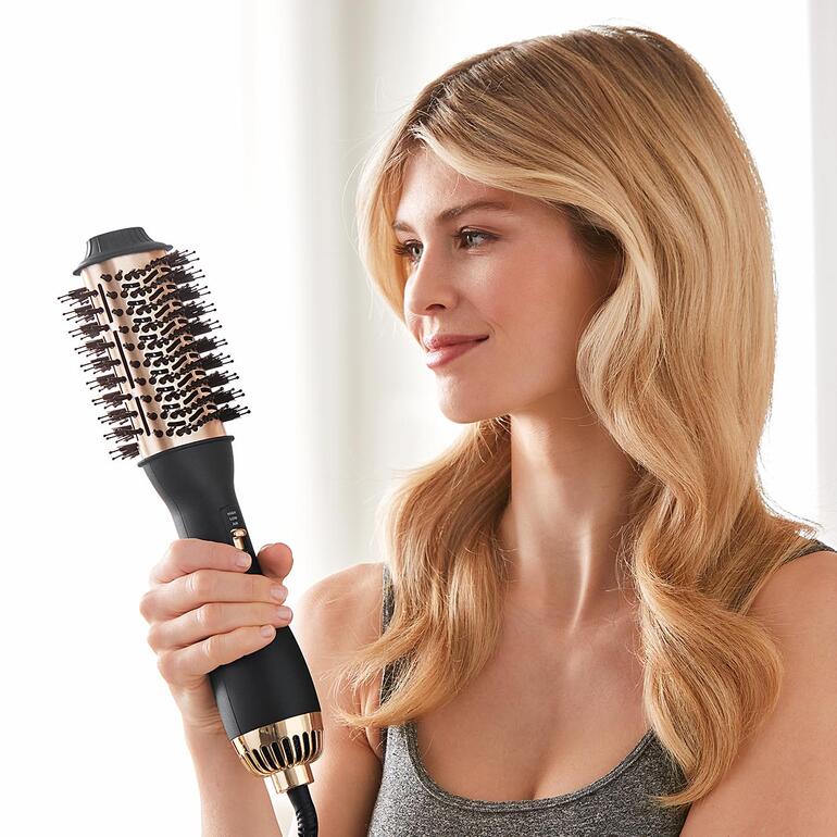 Femme tenant une brosse à air chaud 4-en-1 et souriant.