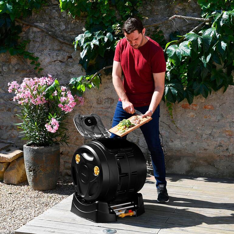 Homme apportant des déchets de cuisine à un composteur à tambour 2-en-1 dans le jardin.